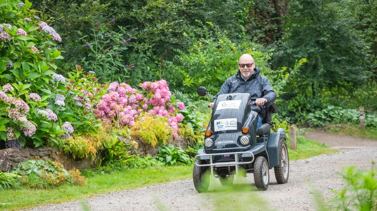 Visitor driving a black tramper mobility vehicle down a path at Fyne Court